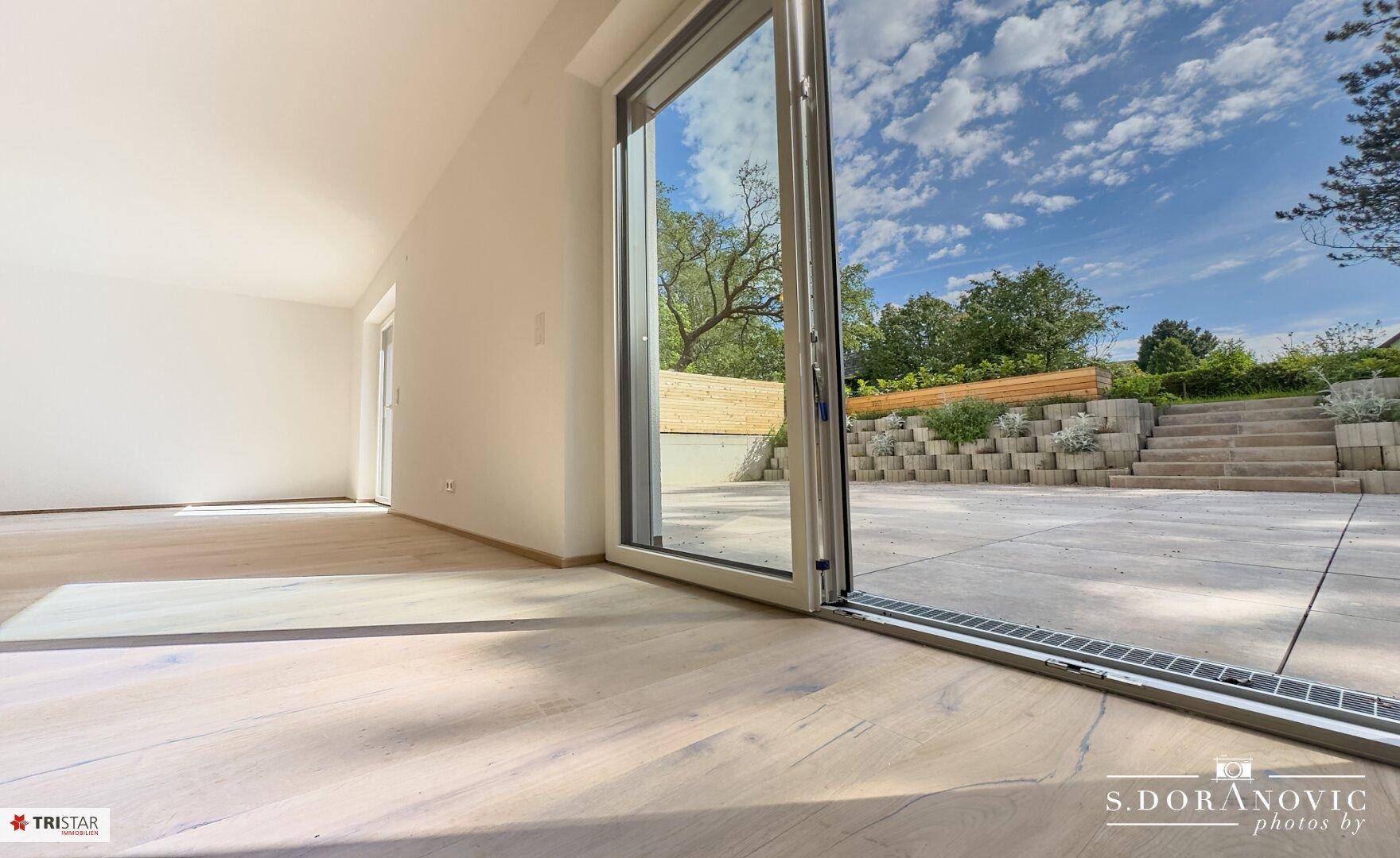 Heller Wohnraum mit Holzboden und direktem Zugang zur großen Außenterrasse und Garten.