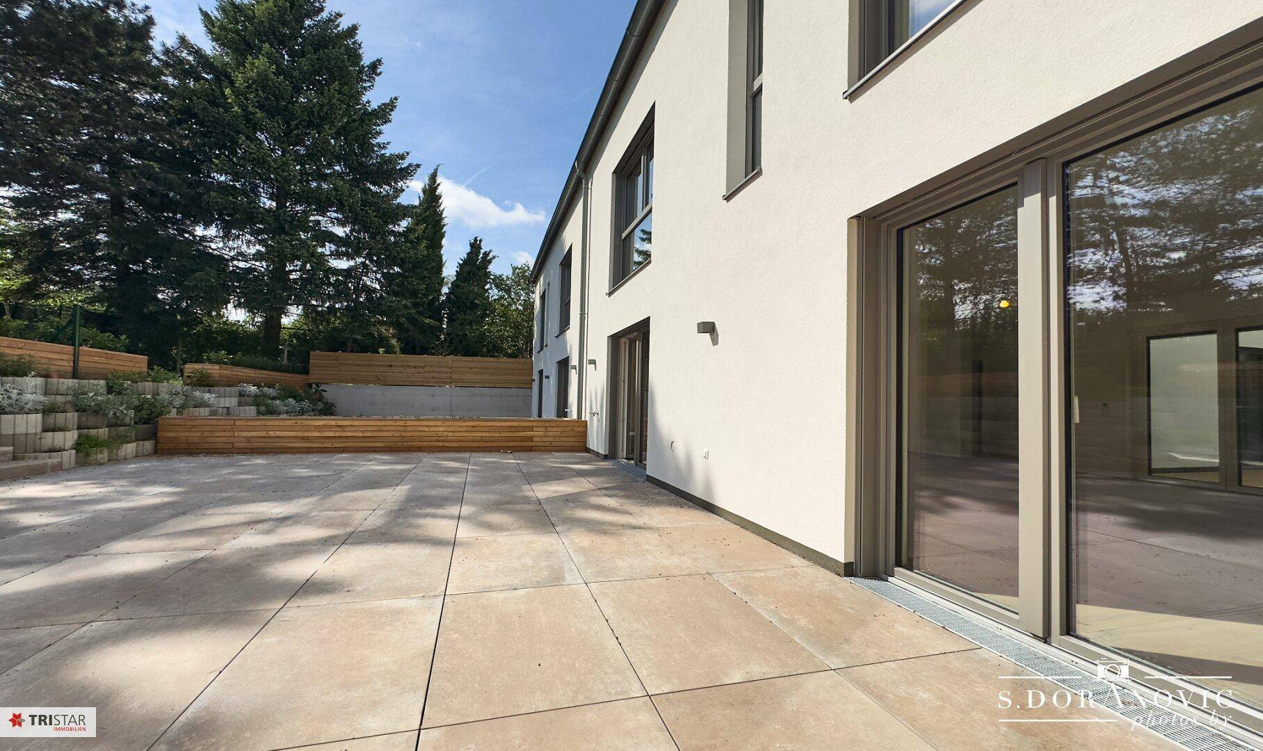 Geräumige, gepflasterte Terrasse am Haus mit großen Schiebetüren und Blick ins Grüne.