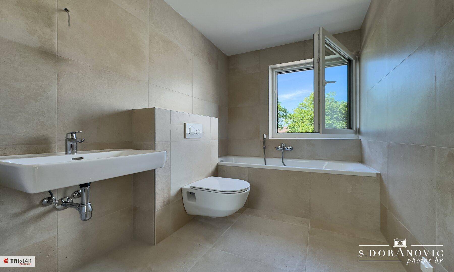 Helles Badezimmer mit Badewanne, Einzelwaschbecken und Wand-WC, modern gefliest.