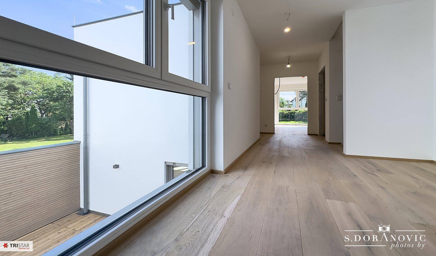 Heller Flur mit Holzboden und Blick durch ein großes Fenster auf die Außenterrasse.