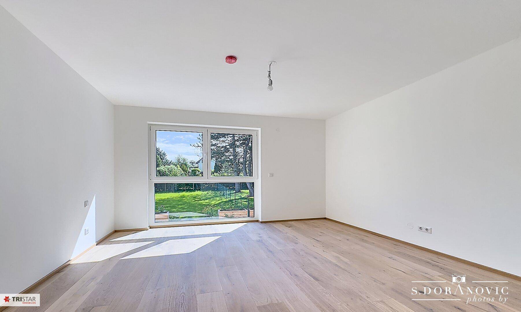 Helles Schlafzimmer mit Holzboden und großem Fenster, das viel Tageslicht hereinlässt.