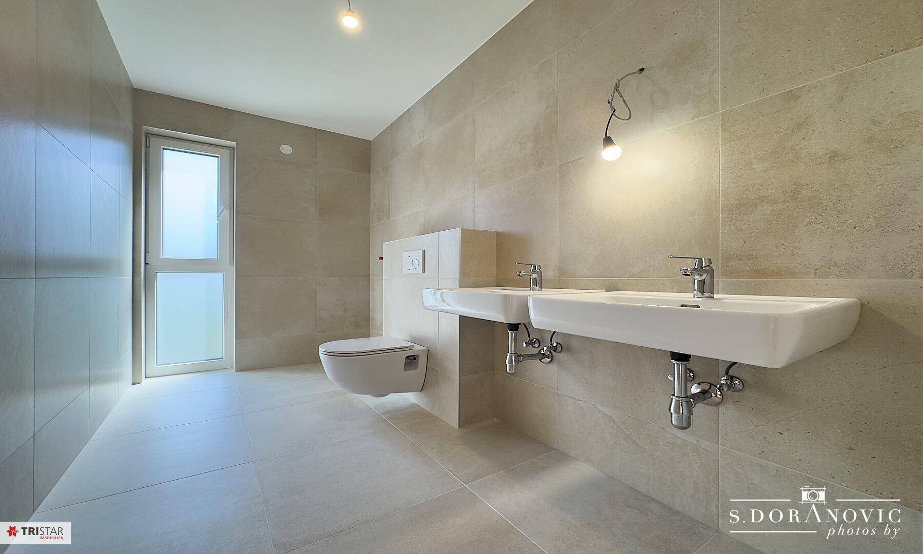 Modernes Badezimmer mit doppelten Waschbecken, Wand-WC und großen Fliesen.