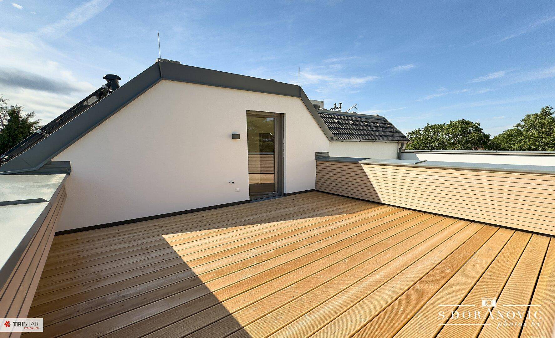 Weitläufige Dachterrasse mit Holzdielen und Zugang zu einem Innenraum, perfekt für sonnige Tage.