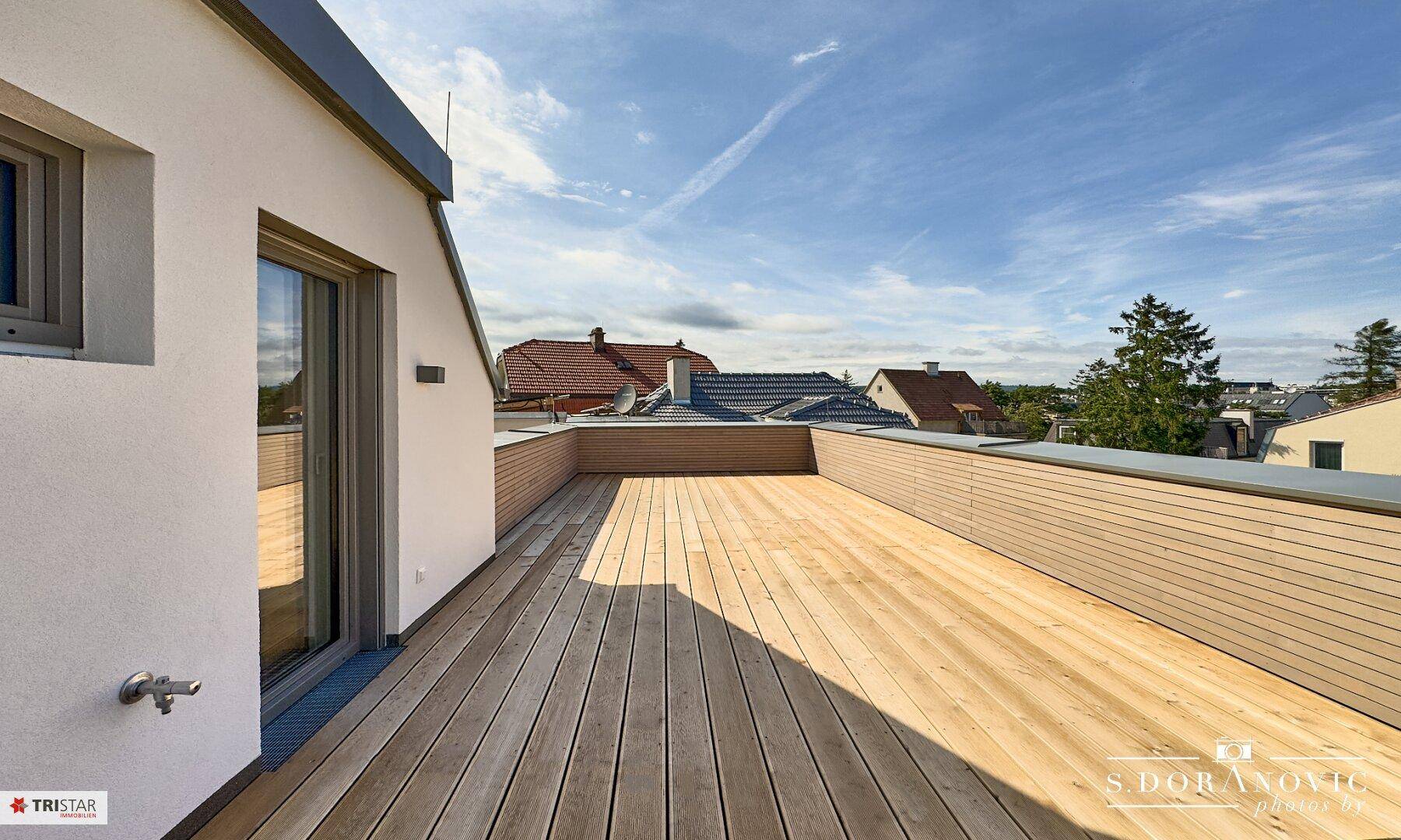 Großzügige Dachterrasse mit Holzbelag und weitem Blick über die Dächer und Baumwipfel.