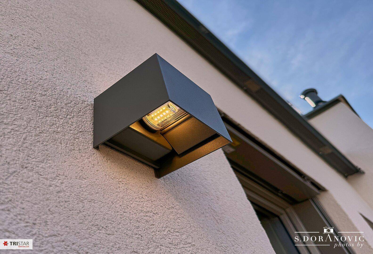 Moderne Außenwandleuchte mit warmem Licht, montiert an der Fassade des Gebäudes.