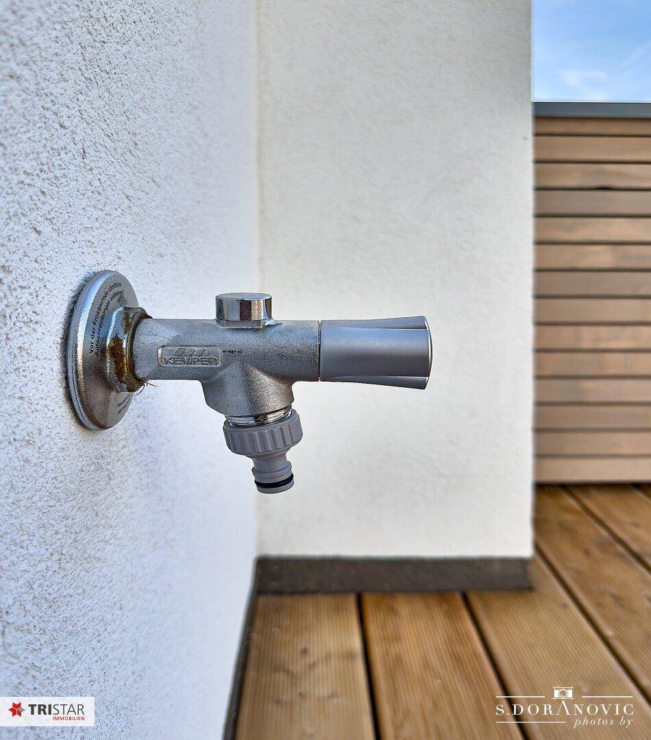 Praktischer Außenwasserhahn an der Fassade, ideal für die Gartenbewässerung oder Reinigung.