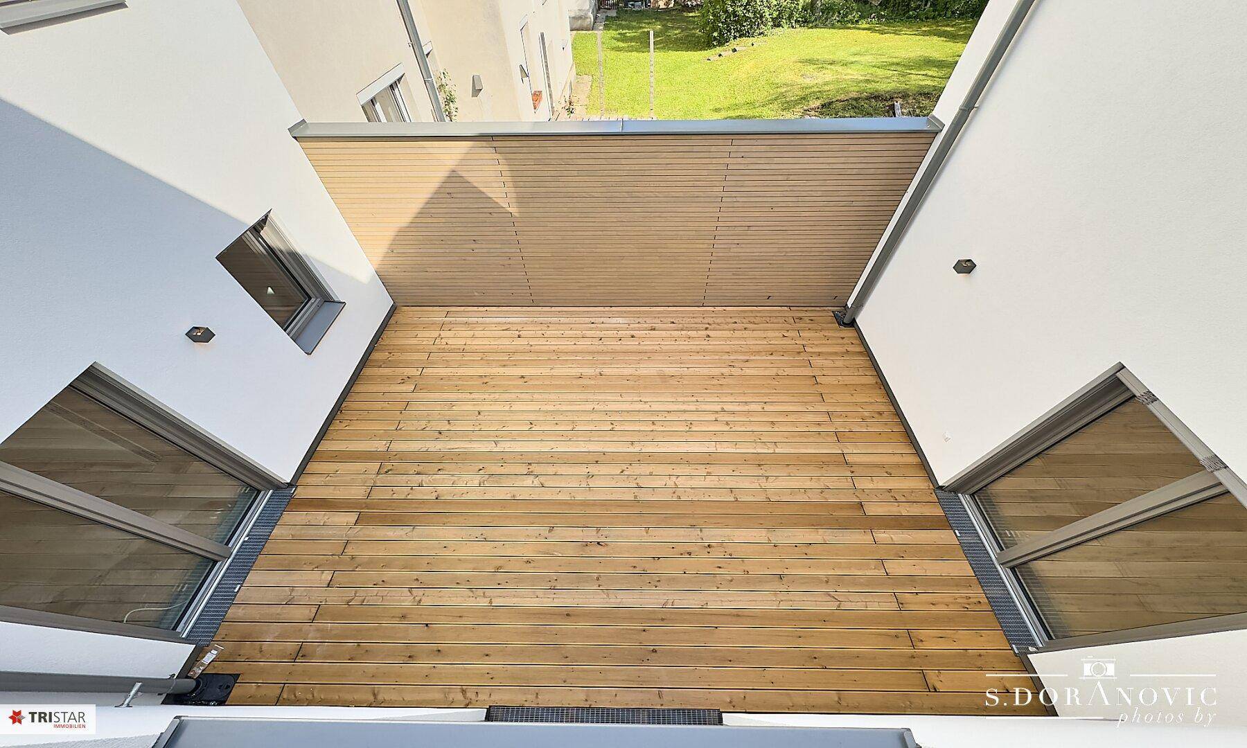 Weitläufige Holzterrasse zwischen Gebäudeteilen, bietet viel Platz im Freien.