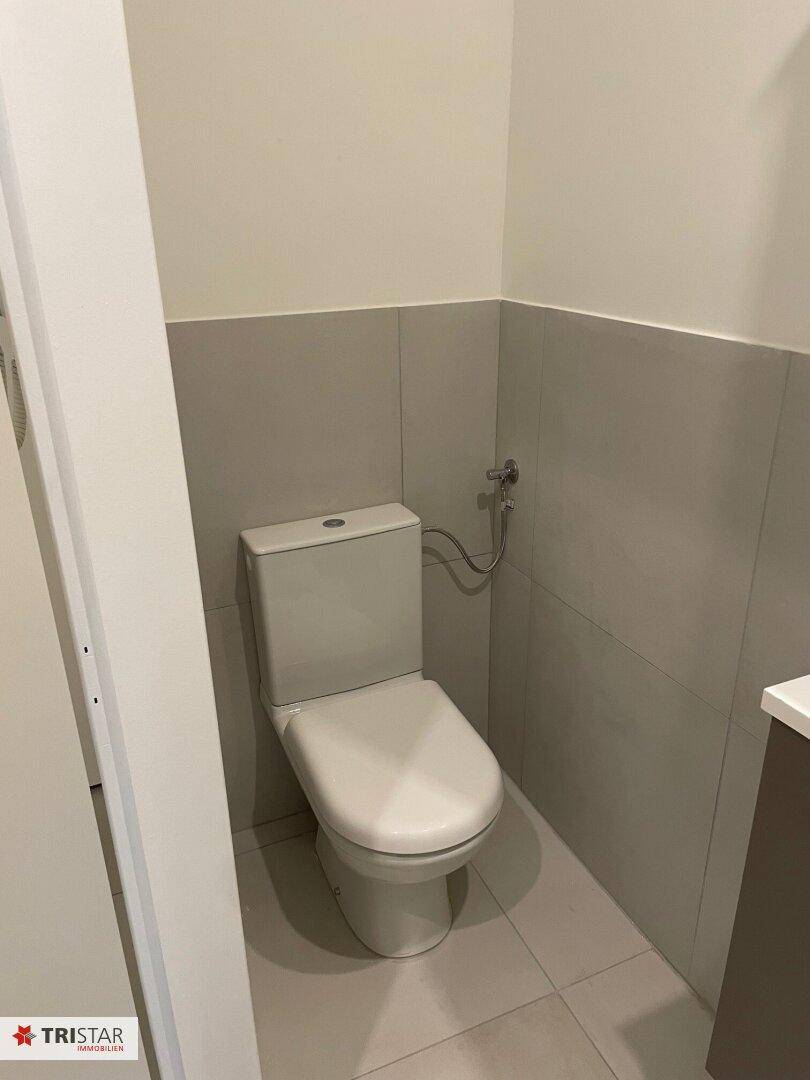 Modernes WC mit Toilette und hellen Fliesen an Wänden und Boden.