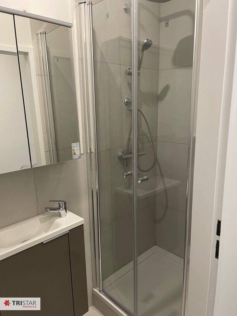 Helles Badezimmer mit moderner Duschkabine, Waschbecken und Spiegelschrank.