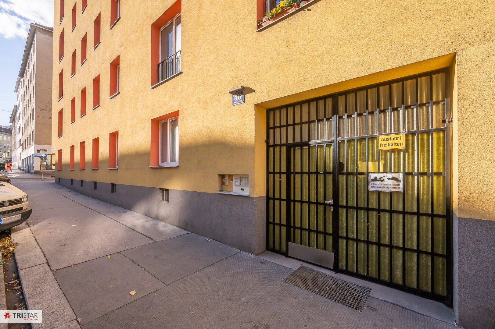 Eingang zur Tiefgarage des Gebäudes mit einem Metalltor und Hinweisschildern.