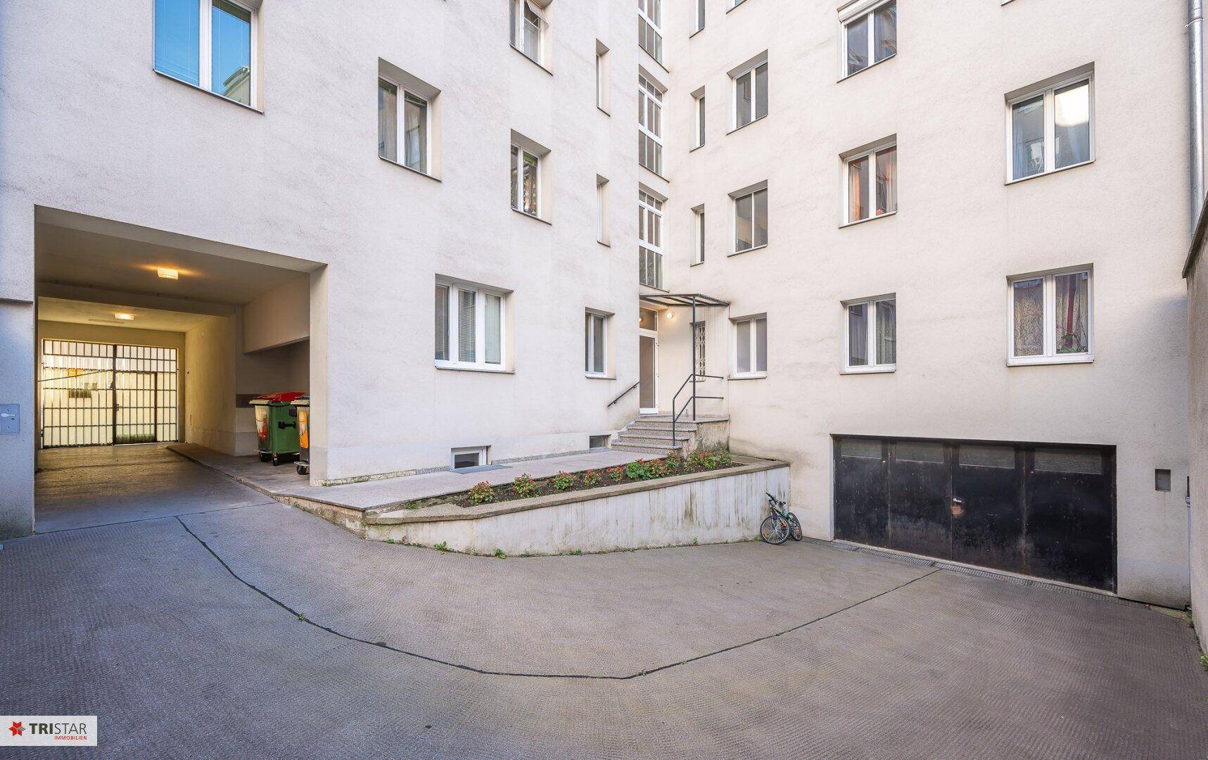 Innenhof eines Gebäudekomplexes mit Zufahrt zu Garagen und einem Durchgang.