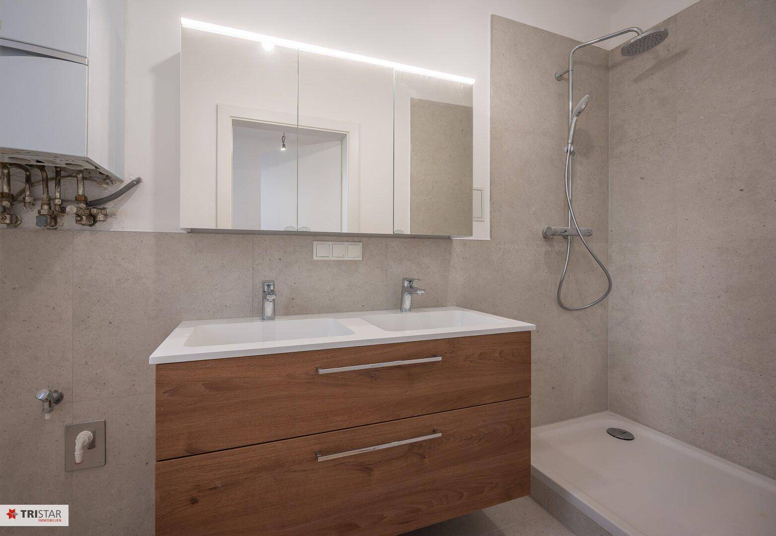 Modernes Badezimmer mit Doppelwaschbecken, beleuchtetem Spiegelschrank und ebenerdiger Dusche.