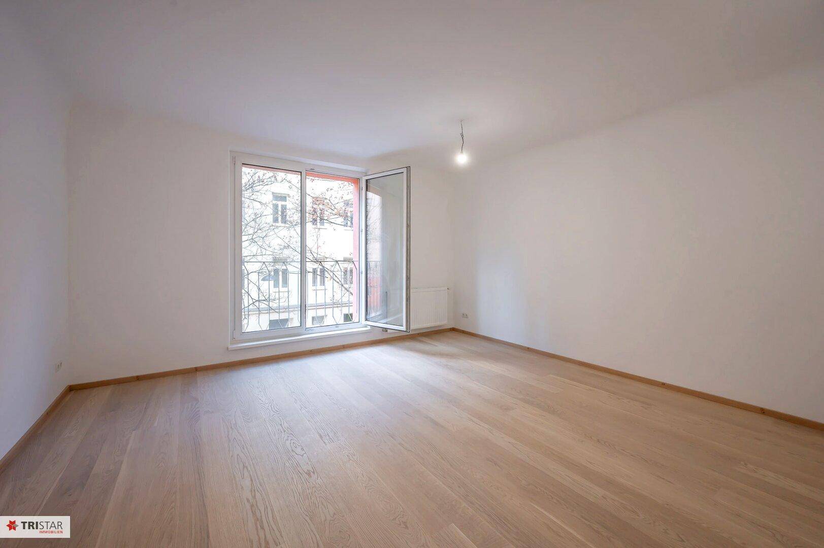 Helles Zimmer mit Parkettboden und französischem Balkon, bietet viel Tageslicht.