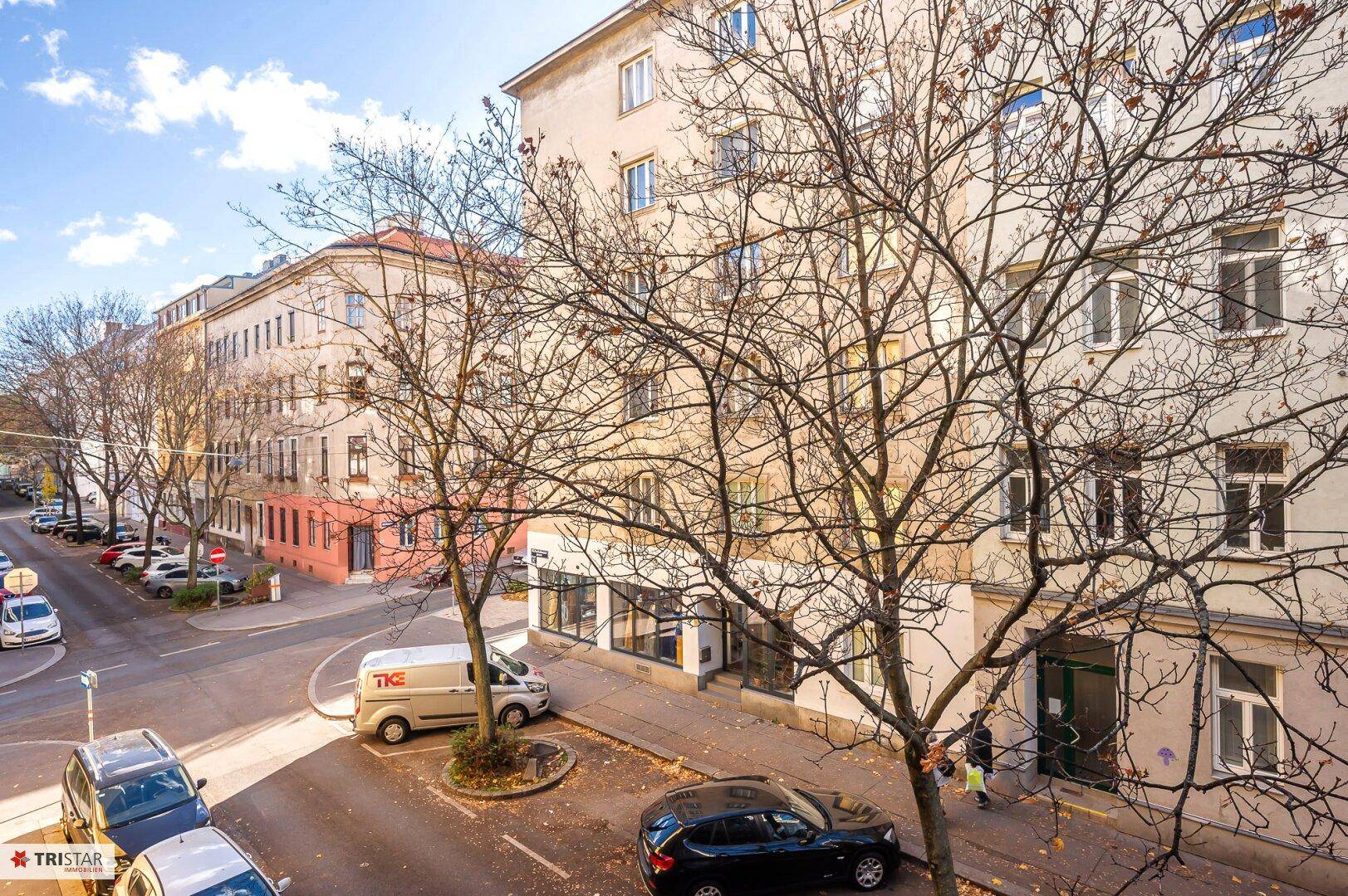 Blick auf eine belebte Straße mit parkenden Autos und umliegenden Gebäuden.