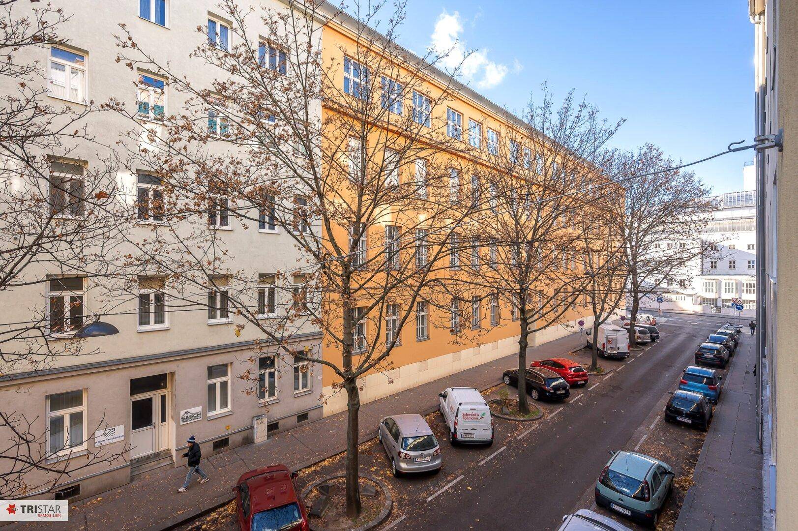 Weitblick über die Straße mit parkenden Fahrzeugen und der Fassade des gegenüberliegenden Gebäudes.