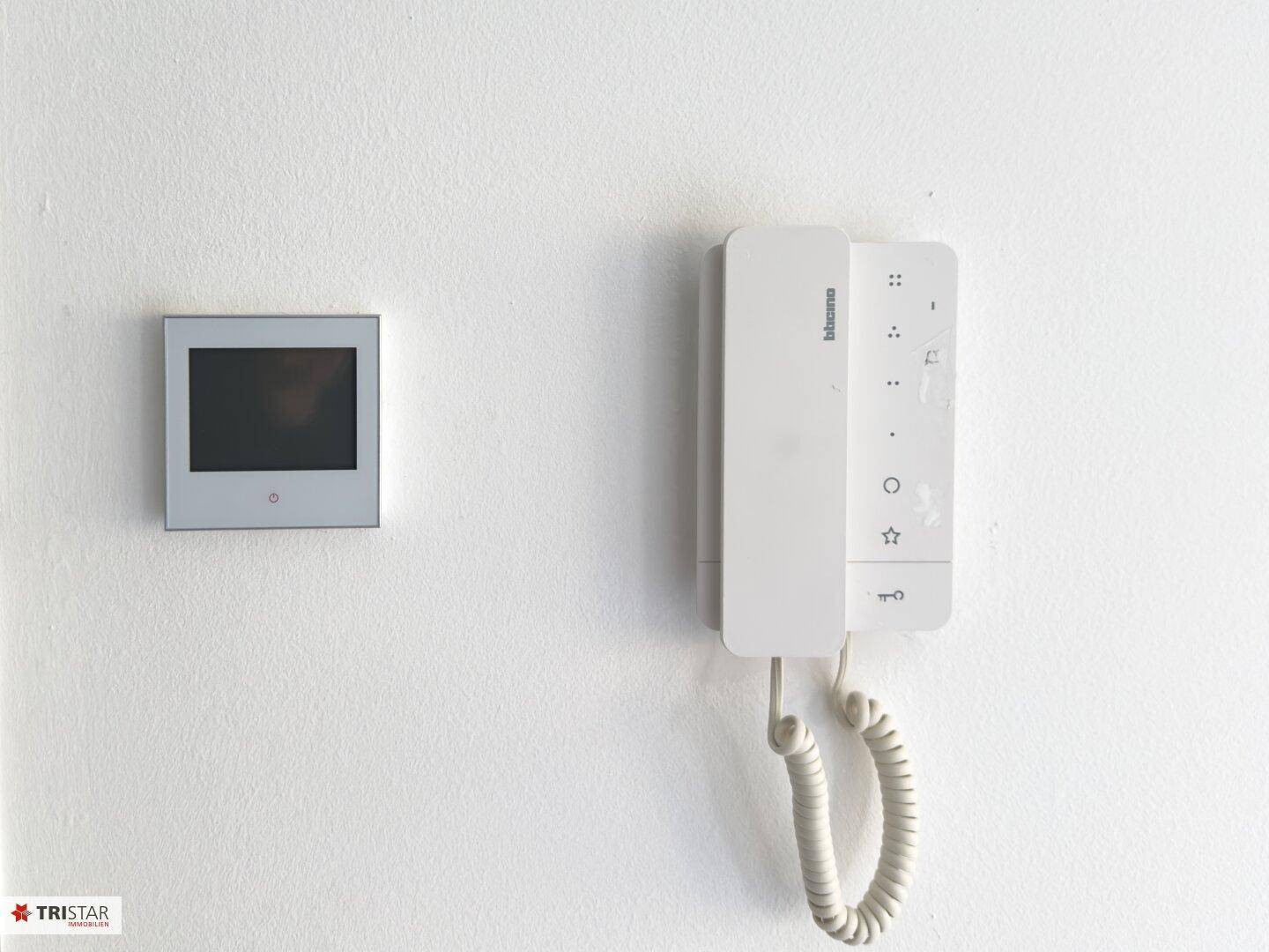 Moderne Gegensprechanlage mit Bildschirm und Telefonhörer an einer weißen Wand installiert.