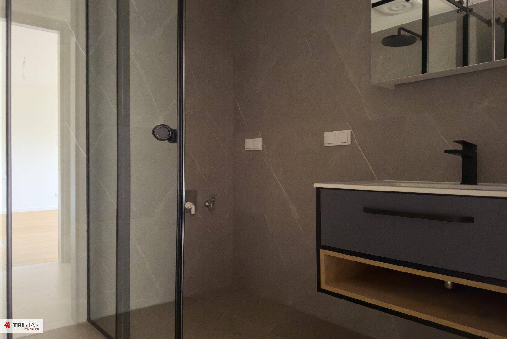 Elegantes Badezimmer mit großformatigen Fliesen, modernem Waschtisch und Regendusche.