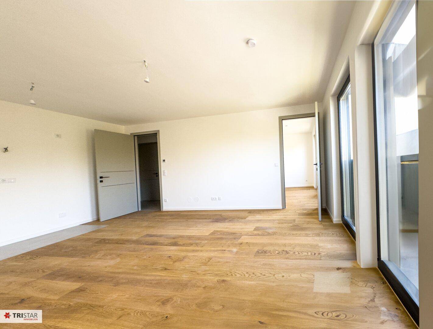 Lichtdurchfluteter Raum mit Holzboden und großen Fenstern, die viel Tageslicht hereinlassen.