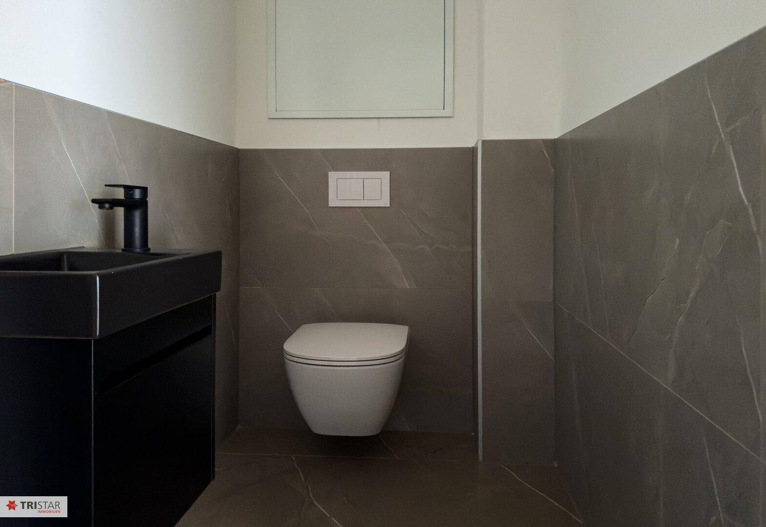 Modernes Gäste-WC mit Wand-WC, kleinem Waschtisch und dunklen Fliesen.