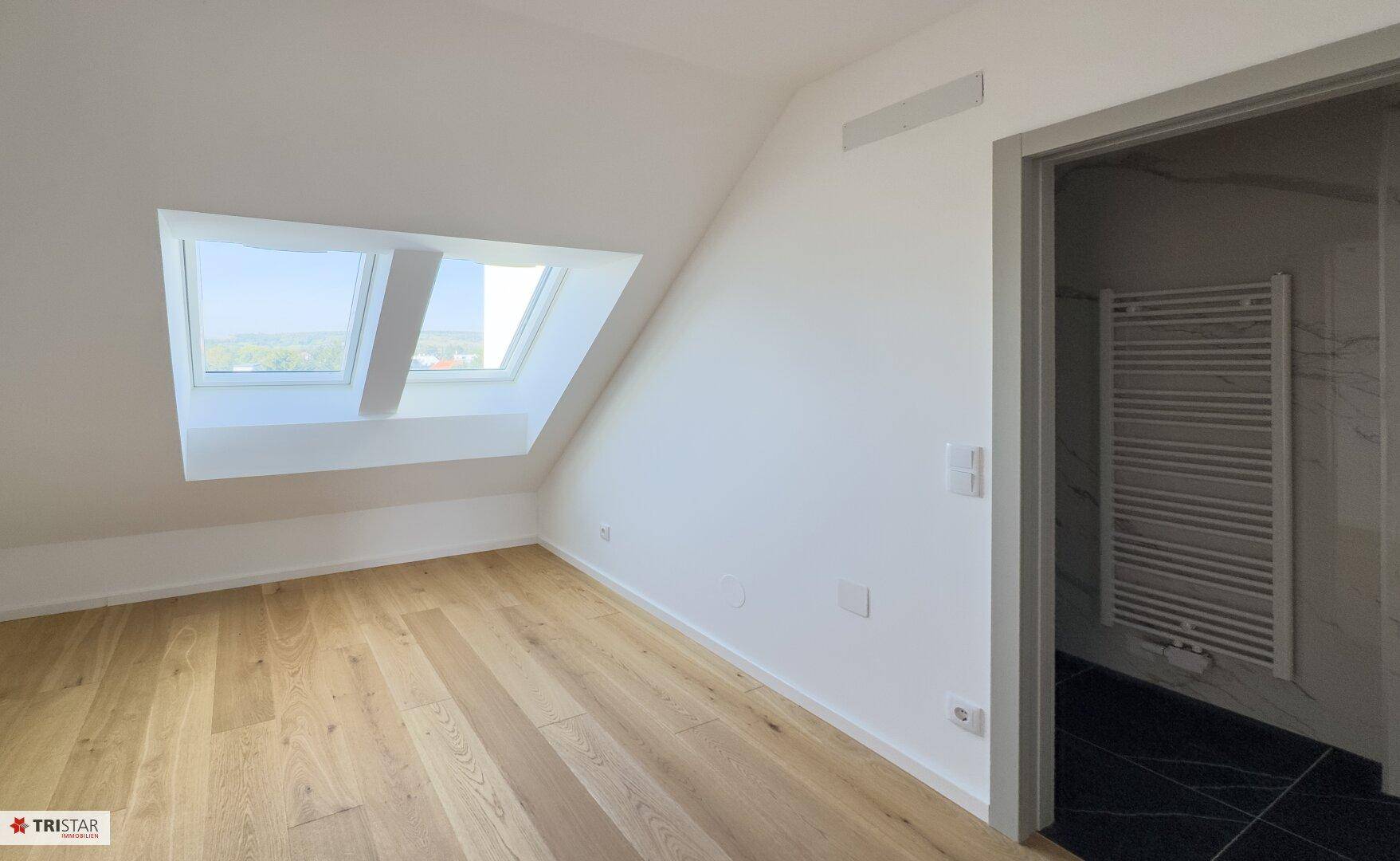 Helles Schlafzimmer mit Holzboden und Dachfenster, das viel Tageslicht in den Raum bringt.