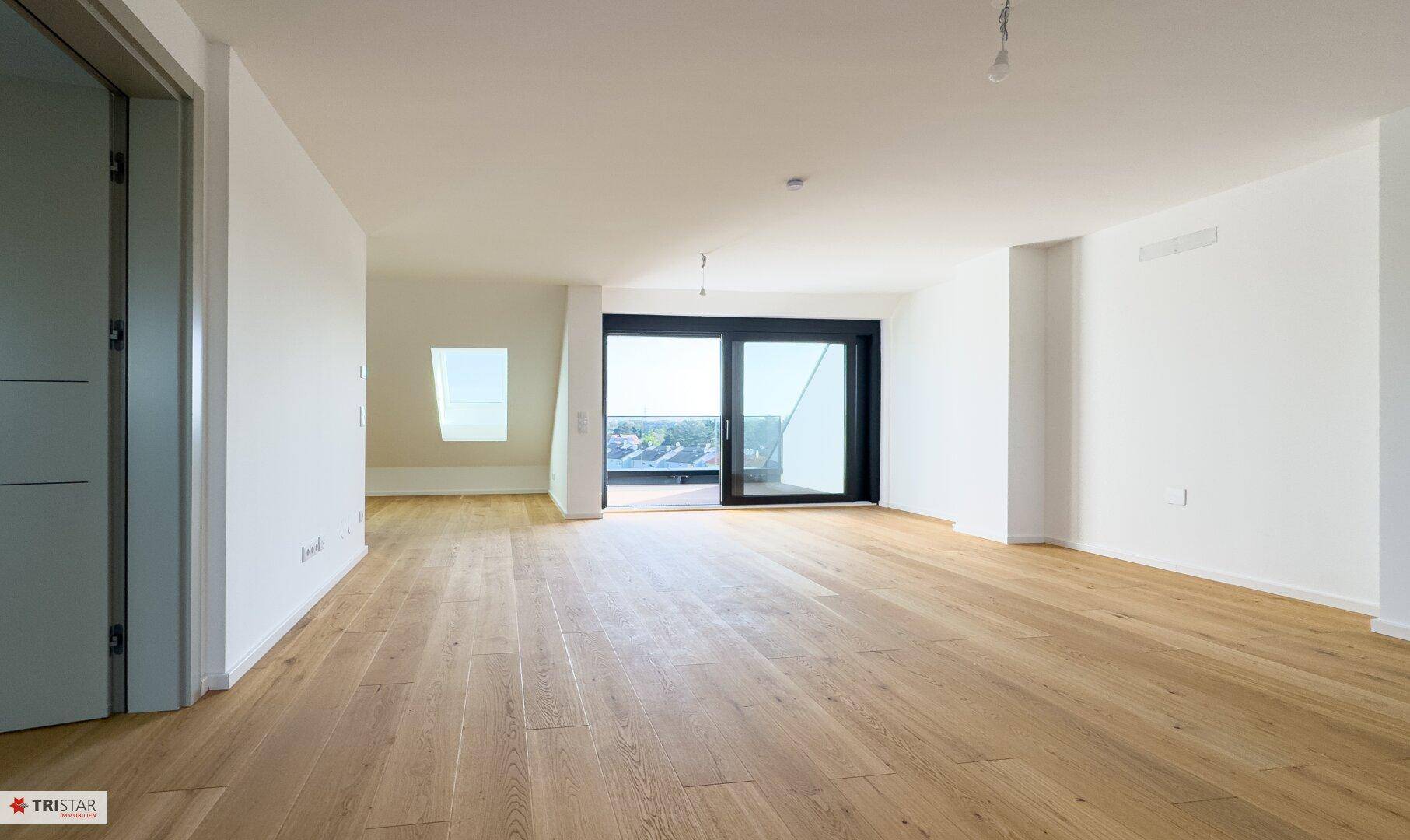 Geräumiger, heller Wohnbereich mit Holzboden und großen Fenstern, die viel Tageslicht hereinlassen.