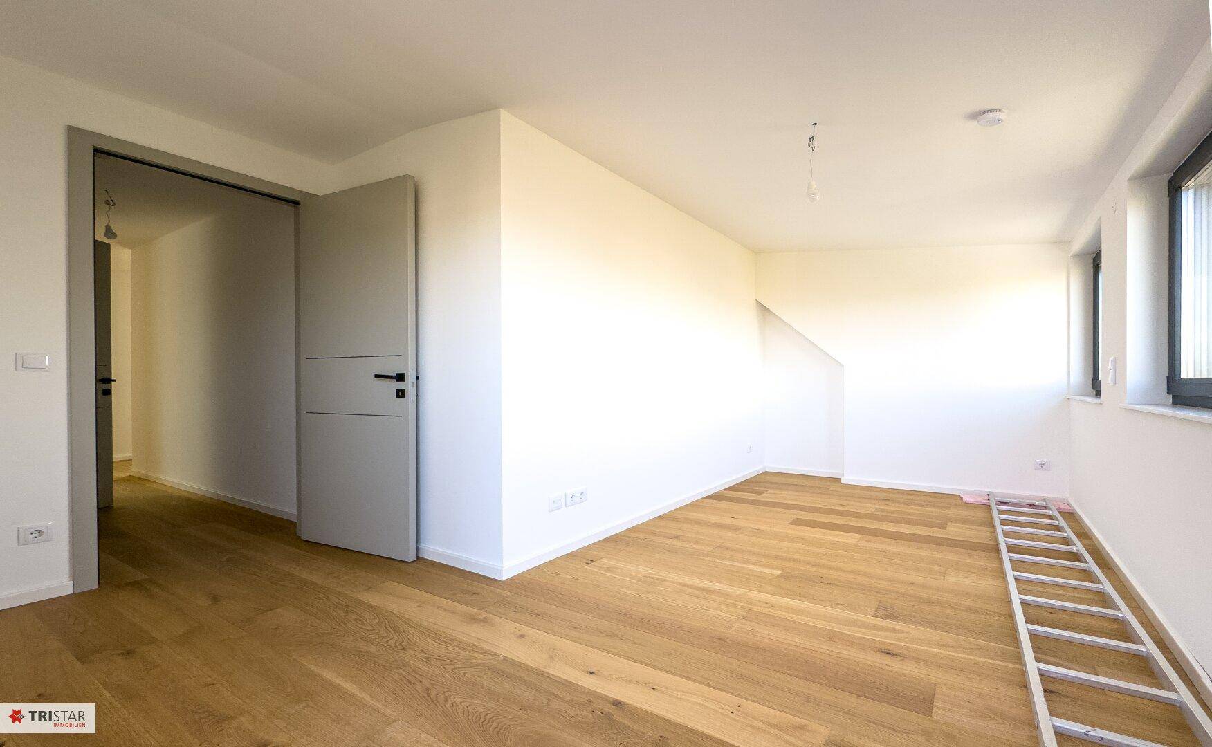 Heller Raum mit Holzboden und Fenstern, die einen weiten Blick auf die Umgebung bieten.