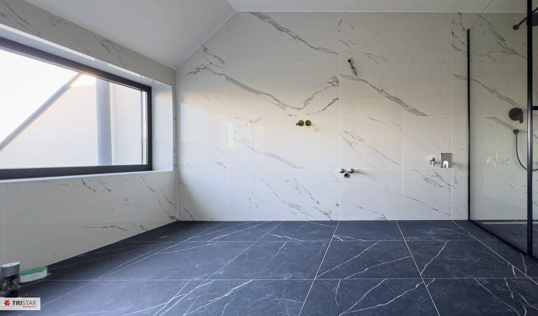 Geräumiges Badezimmer mit eleganten Marmorfliesen und einem großen Fenster, das viel Licht spendet.