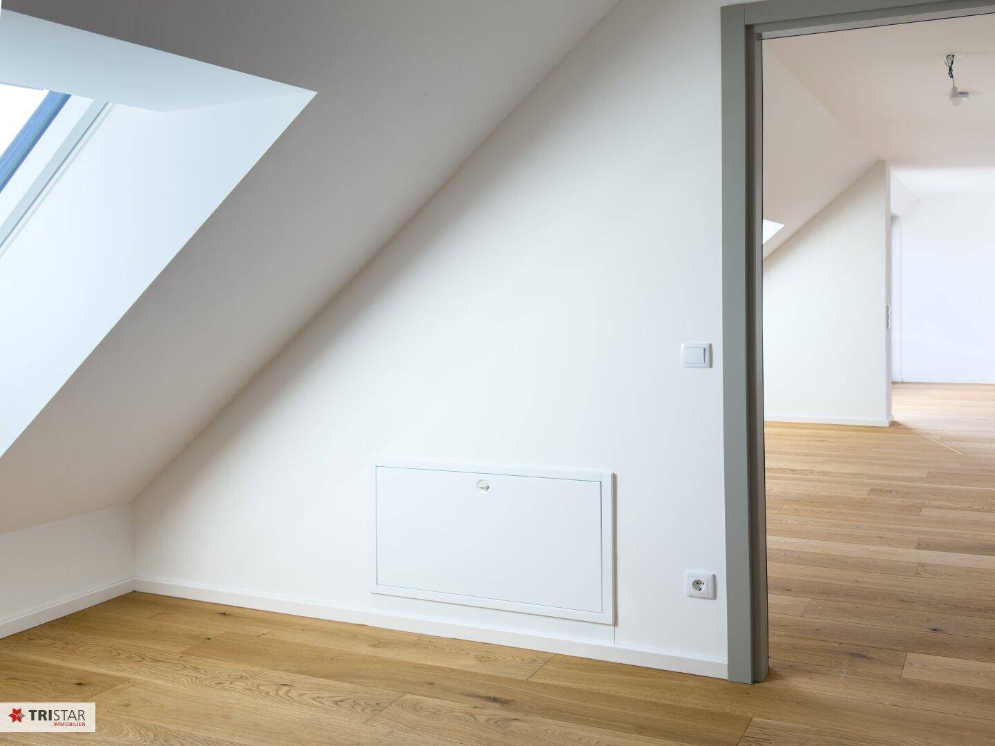 Helles Zimmer mit Holzboden und Dachfenster, bietet zusätzlichen Stauraum durch eine Wandnische.