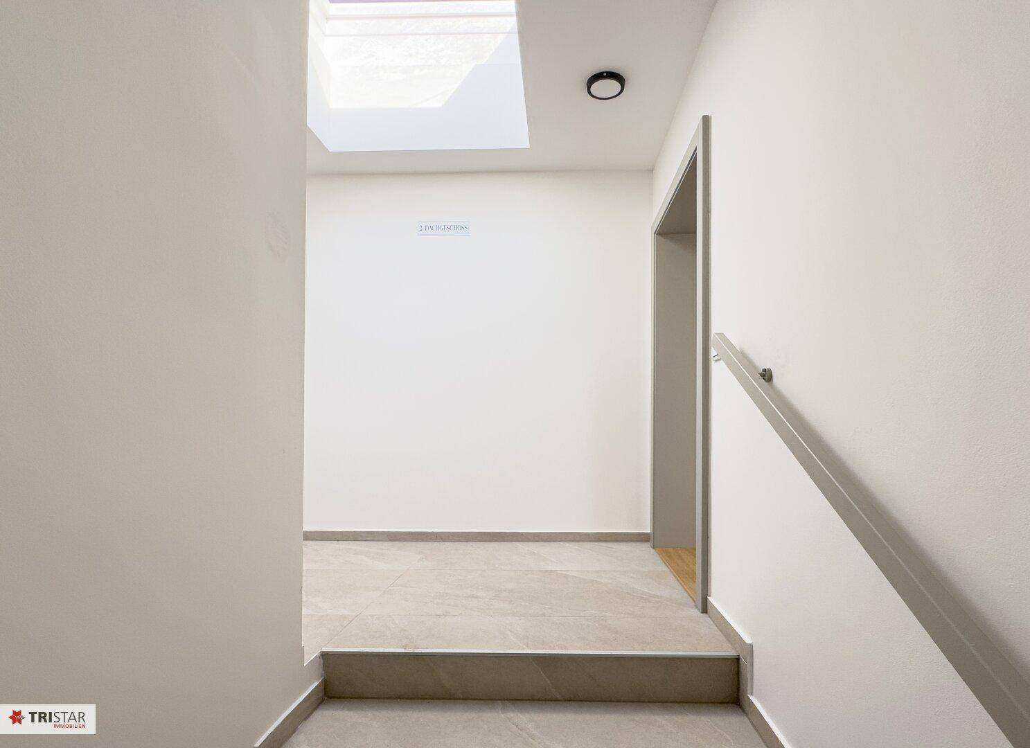 Heller Treppenabsatz mit Fliesenboden und einem Dachfenster, das den Bereich natürlich beleuchtet.