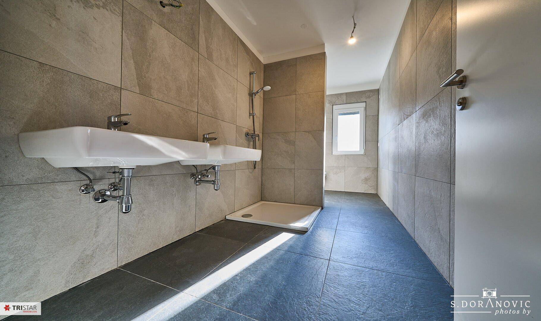 Modernes Badezimmer mit Doppelwaschbecken, begehbarer Dusche und grauen Fliesen.