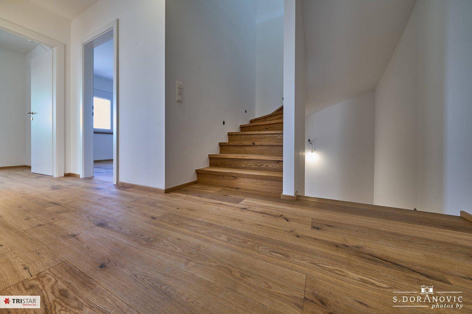 Heller Flur mit Holzboden und einer eleganten Holztreppe, die in die oberen Stockwerke führt.