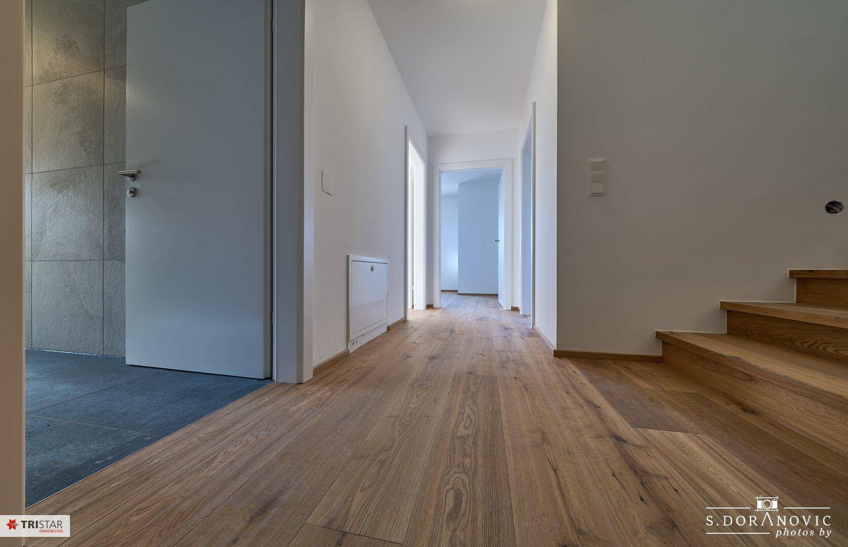 Heller Flur mit Holzboden, der zu weiteren Räumen und einer Treppe führt.