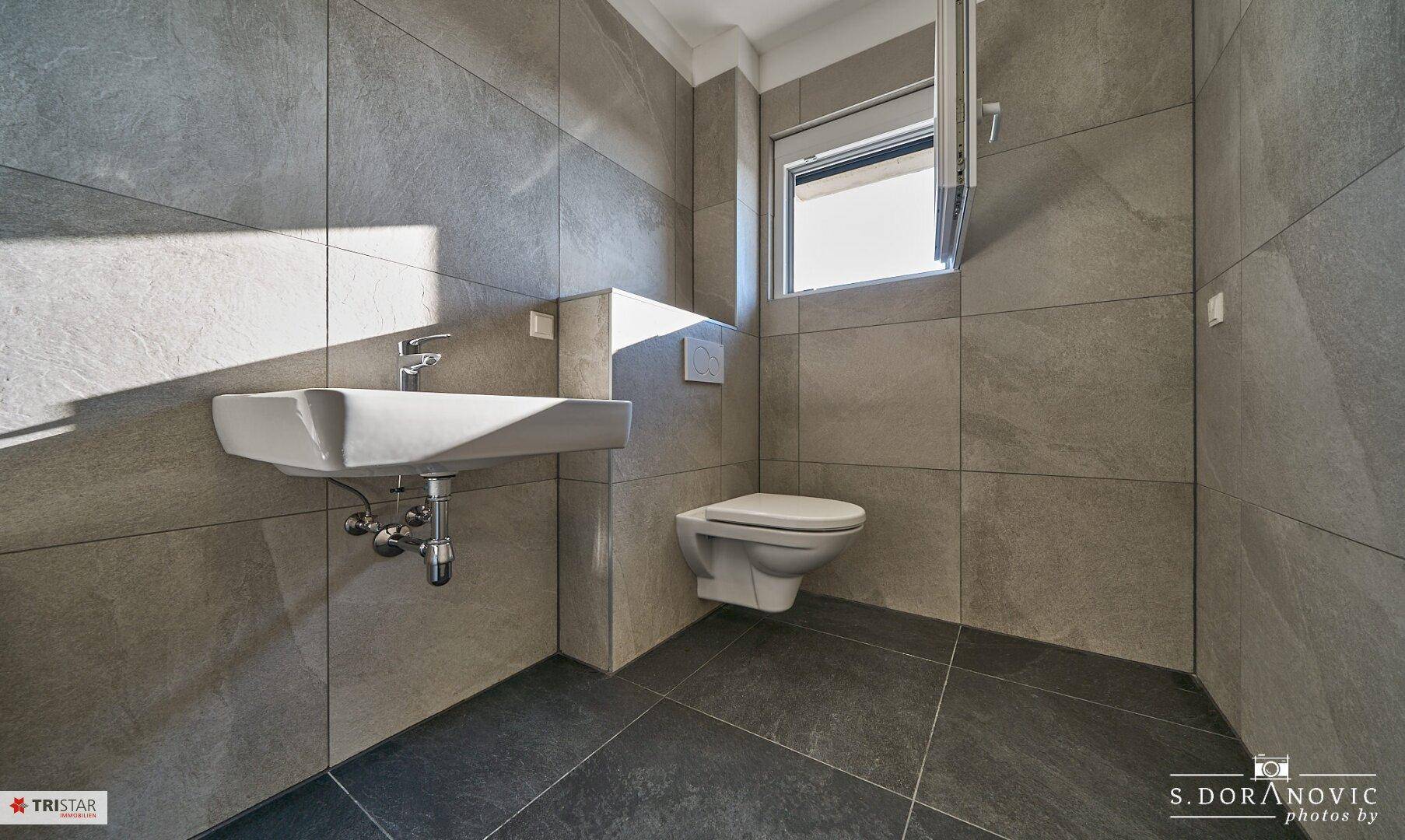 Helles Gäste-WC mit modernem Waschbecken, wandhängender Toilette und Fenster.