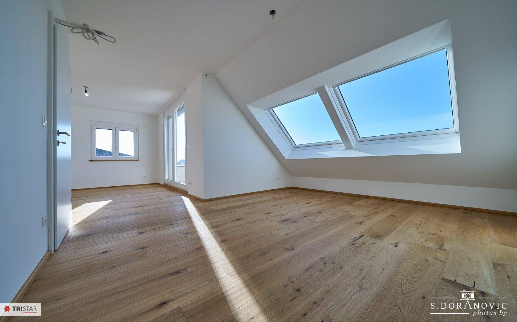 Geräumiger, heller Raum im Dachgeschoss mit Holzboden, Dachfenstern und Zugang zur Terrasse.