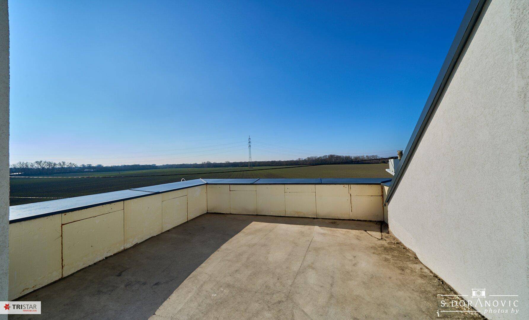 Große, leere Dachterrasse mit weitem Blick über Felder und die umliegende Landschaft.