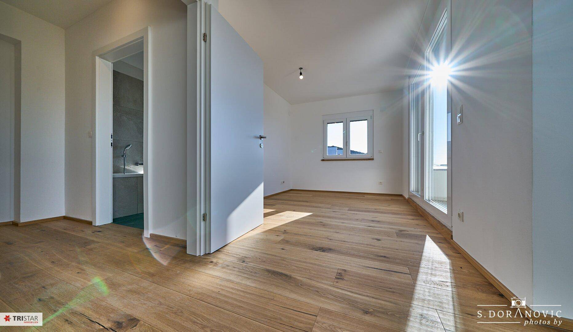 Heller Raum mit Holzboden, Fenster und direktem Zugang zu einem Badezimmer mit Badewanne.