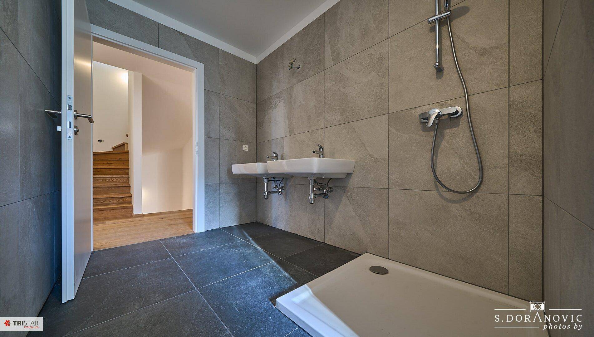 Modernes Badezimmer mit Doppelwaschbecken und Dusche, angrenzend an einen Treppenbereich.