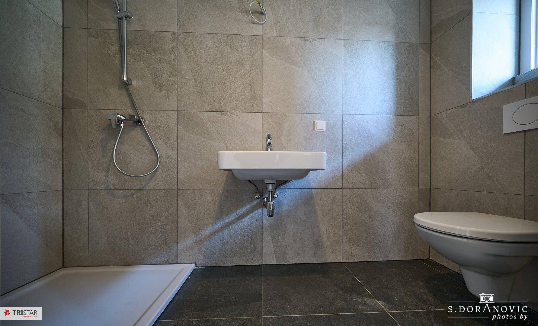 Modernes Badezimmer mit Dusche, Waschbecken und Toilette, hell gefliest.
