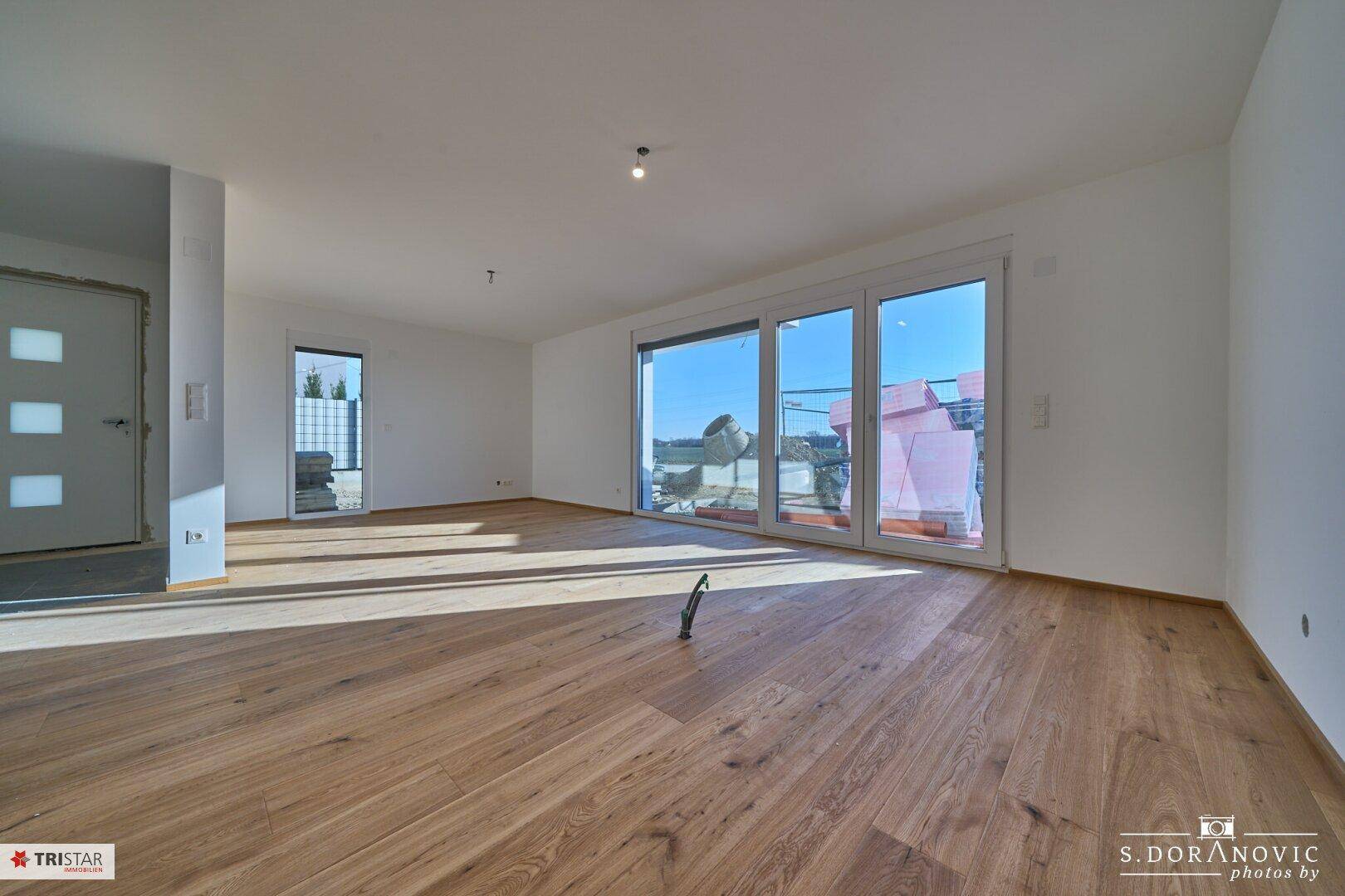Heller Eingangsbereich oder Wohnraum mit Holzboden und großer Glastür zum Außenbereich.
