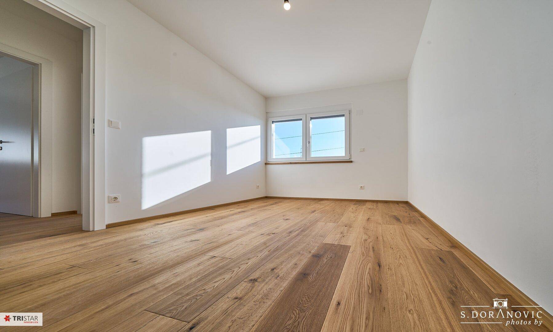 Leerer, heller Raum mit Holzboden und einem Fenster, das für natürliche Belichtung sorgt.