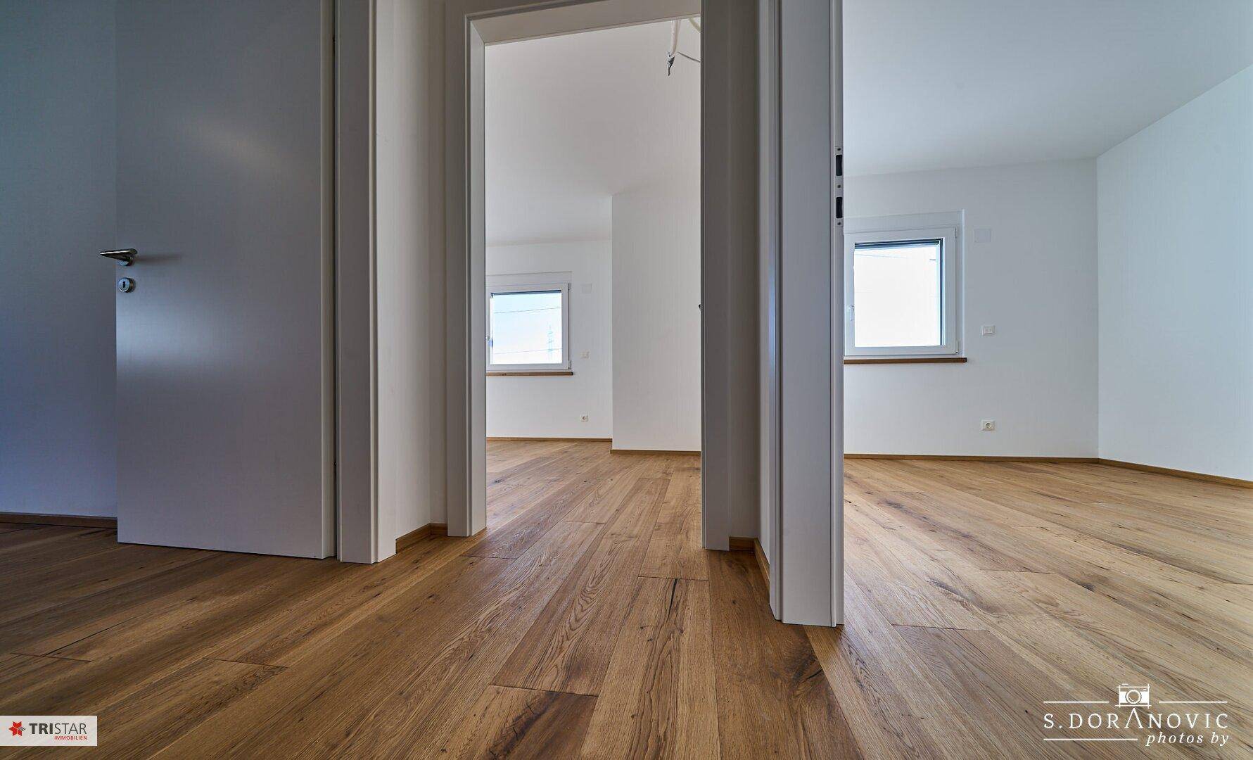 Heller Flur mit Holzboden, der zu weiteren leeren Zimmern führt.