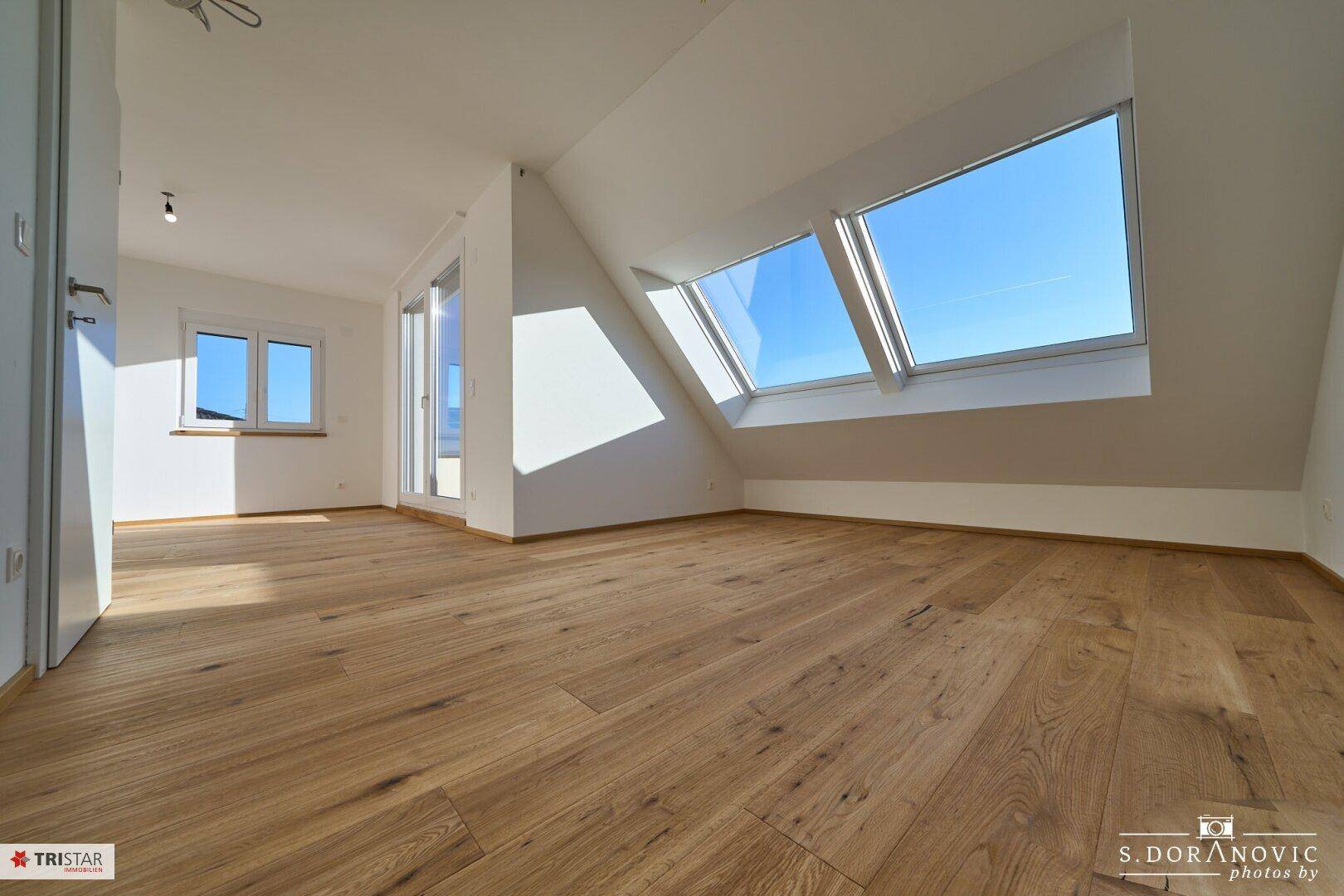 Geräumiger, heller Raum im Dachgeschoss mit Holzboden, Dachfenstern und Zugang zur Terrasse.