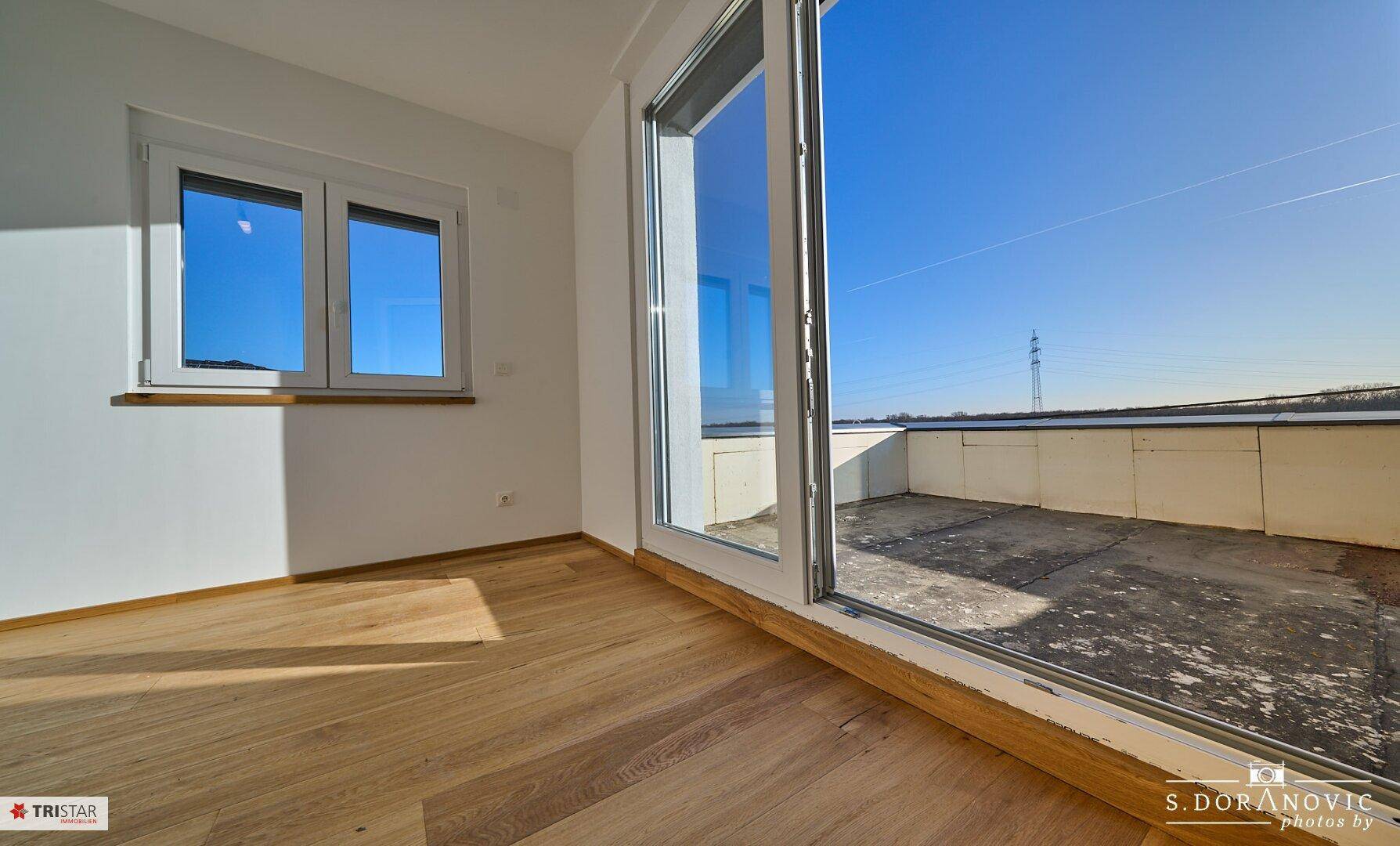 Heller Raum mit Holzboden und Zugang zu einer großen Terrasse mit weitem Blick.