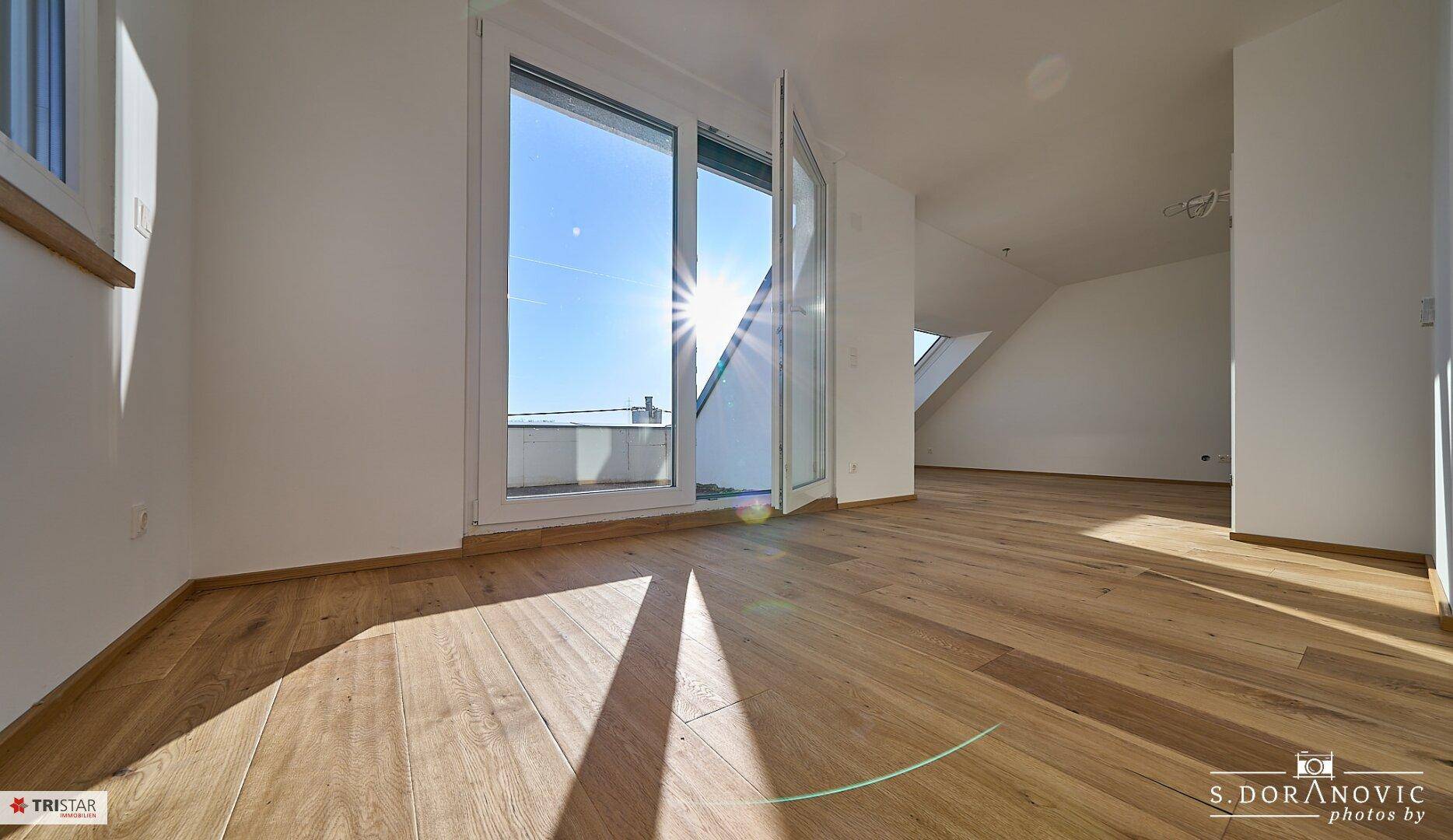 Geräumiger, heller Raum mit Holzboden, Zugang zur Terrasse und schrägen Dachfenstern.