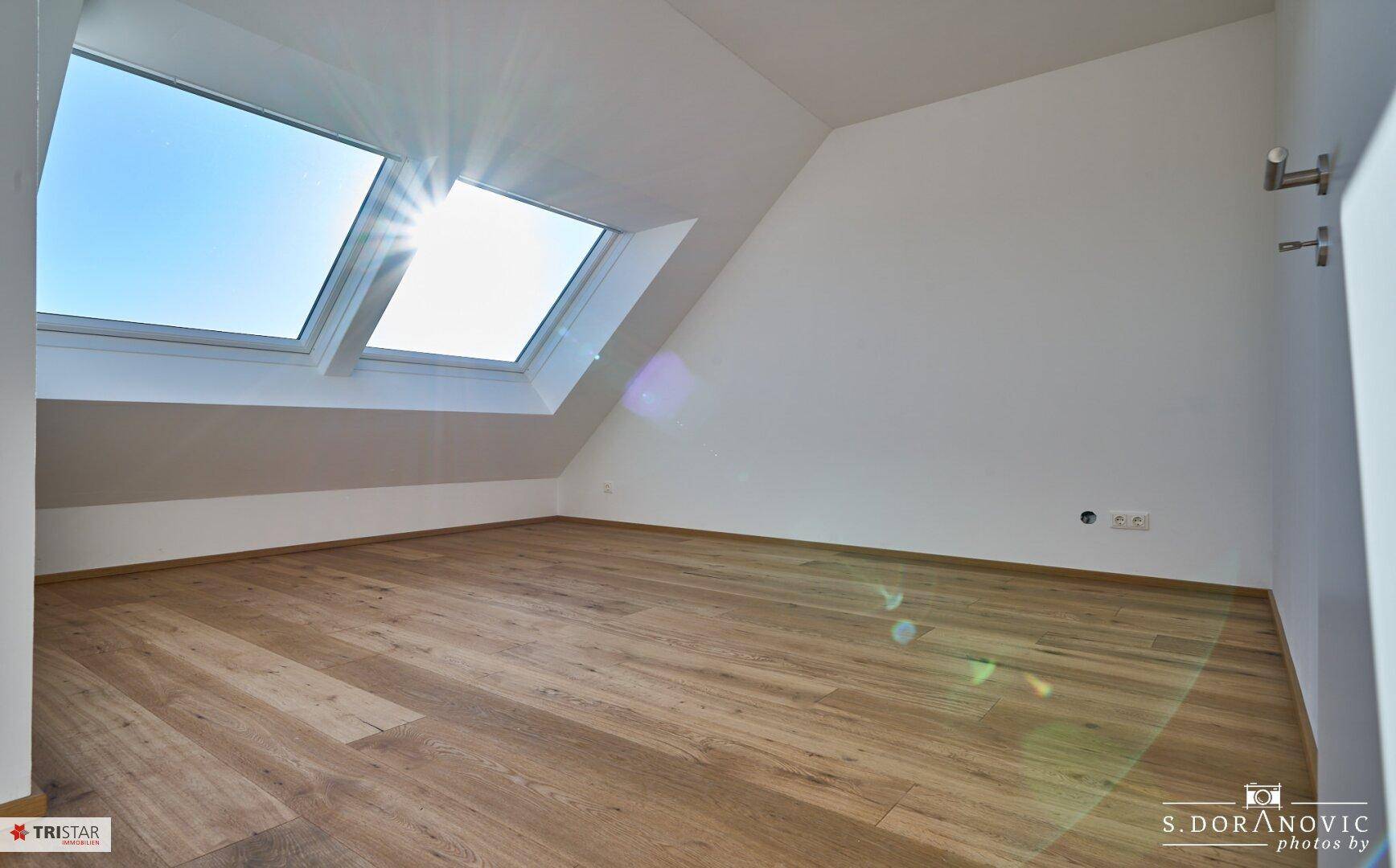 Heller Raum im Dachgeschoss mit Holzboden, Fenster und zwei großen Dachfenstern.