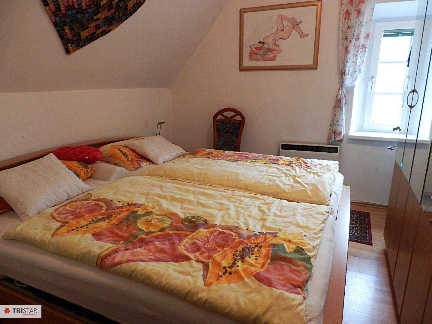 Schlafzimmer im Dachgeschoss mit Doppelbett, Holzfußboden und Fenster mit Vorhängen.