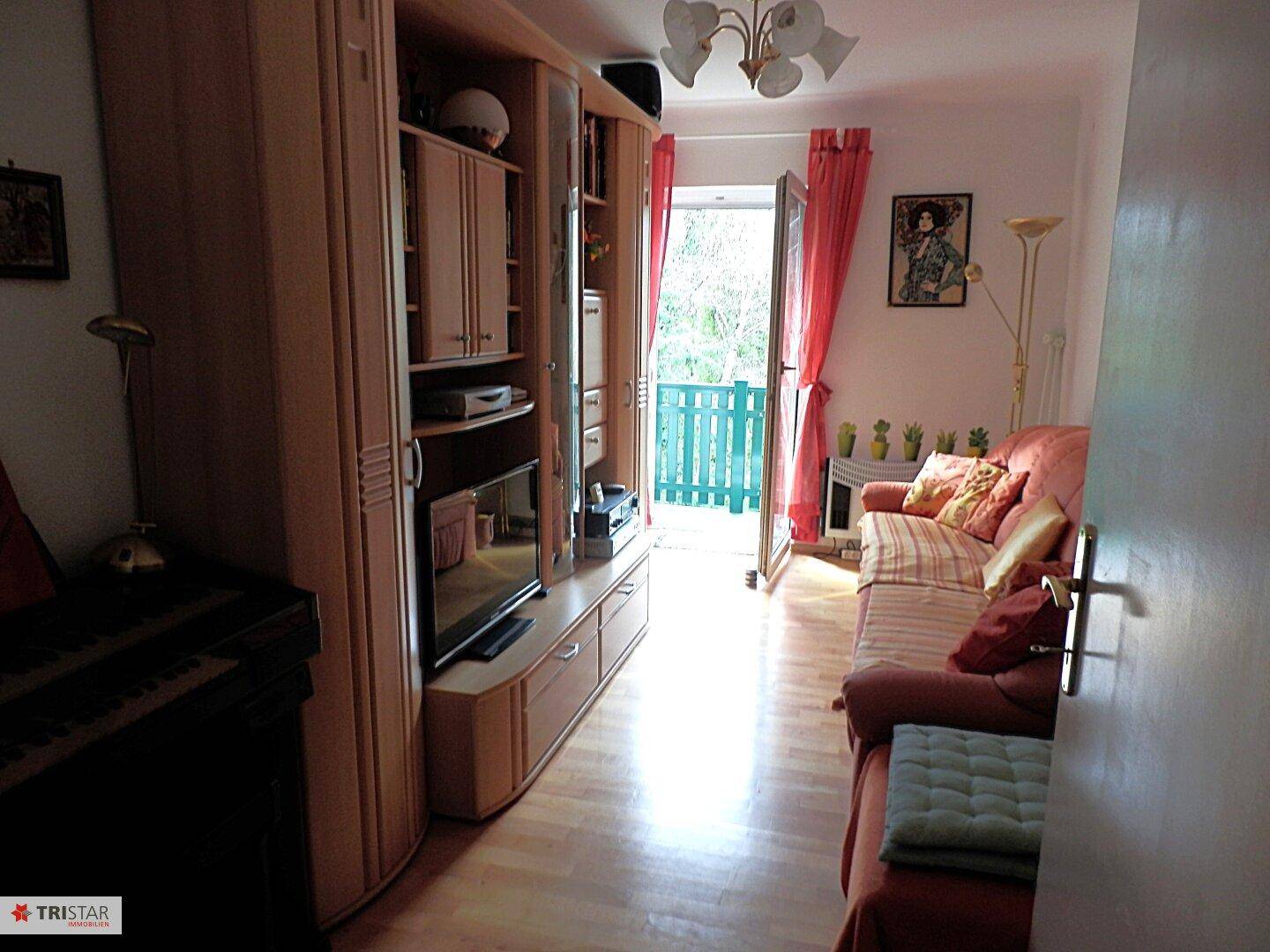 Gemütliches Wohnzimmer mit Sofa, Schrankwand und Zugang zu einem kleinen Balkon.