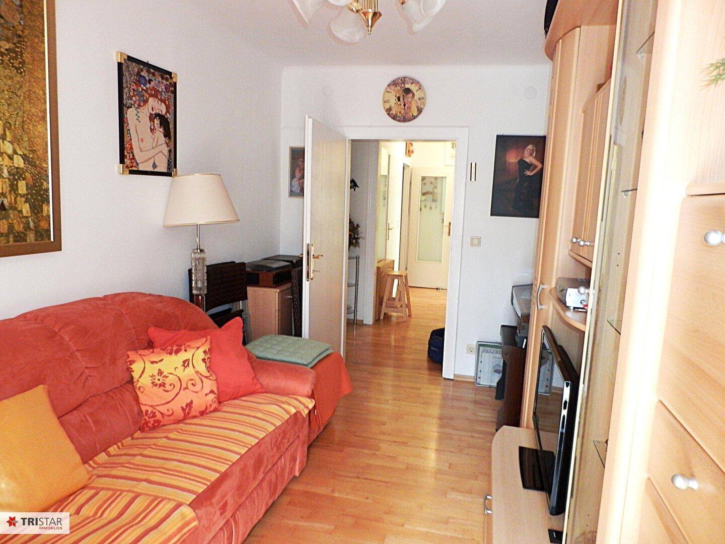 Helles Wohnzimmer mit Sofa, Schrankwand und Durchgang zu einem weiteren Raum.