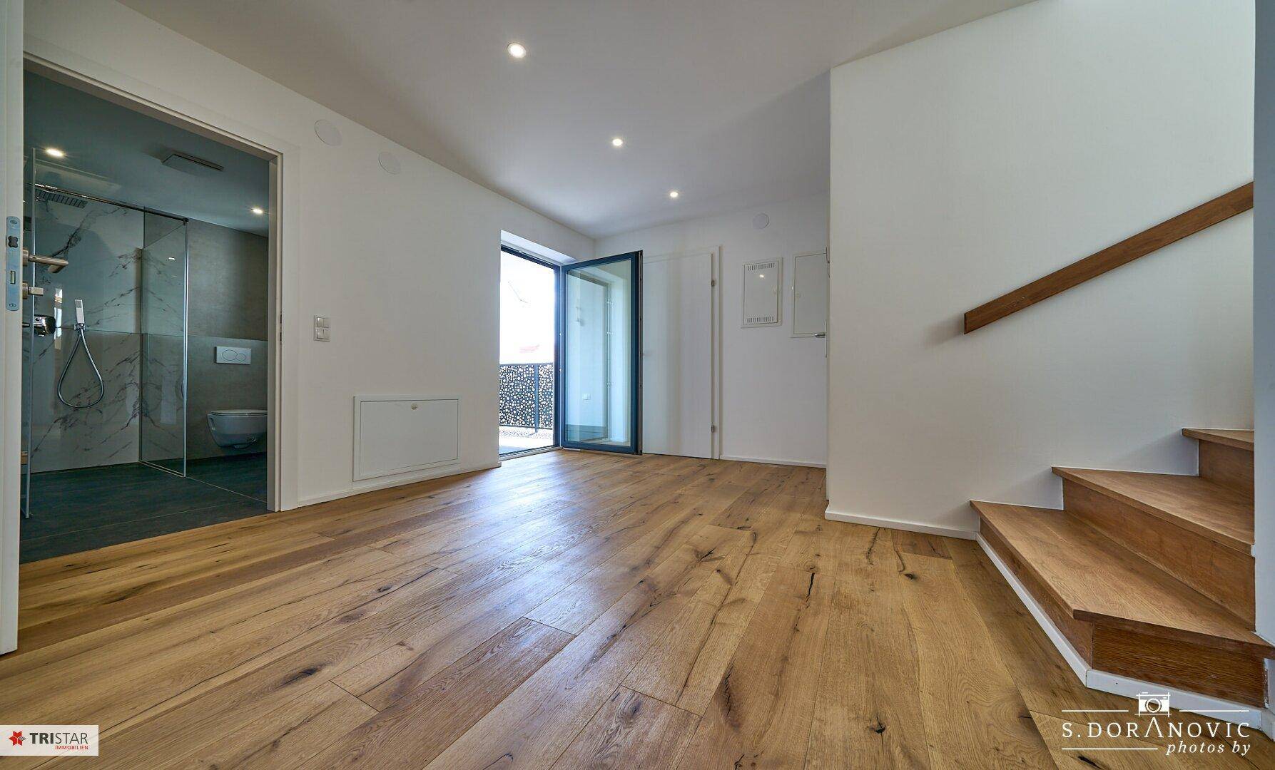 Moderner Flur mit Holzboden, Zugang zum Balkon und Blick auf ein stilvolles Badezimmer.