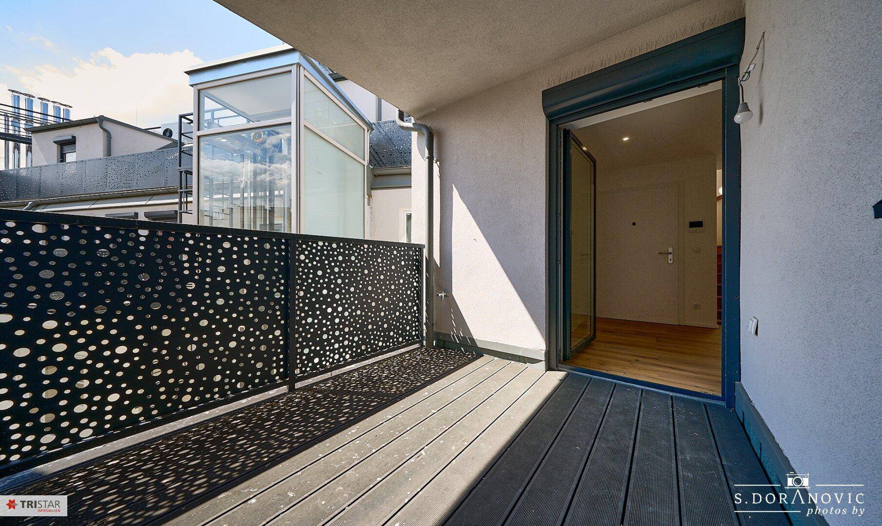 Geräumiger Balkon mit modernem Lochblechgeländer und Holzboden, ideal für Entspannung.